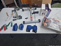 Exercise equipment lot on table showing folding indoor bicycle, push-up bar extender, hand grips, blue padded weights, and Core Secrets workout kit box