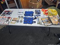 Table display showing assortment of exercise equipment and running magazines on a white folding table. Items include ankle weights, hand weights, grips, runner vests, and multiple magazines.