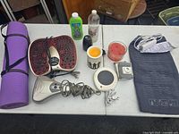 Full shot of all items on table showing yoga mat, foot massager, handheld massager, heating pad, candles, lotion bottles, and small black item
