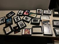 Multiple 5x7 black photo frames laid out on a table with assorted prints, including black and white and color images, some of people, nature, and abstract art.