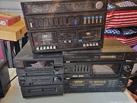 Realistic System 200 double cassette player on top with Sharp combo tuner amplifier double cassette player and Aiwa NSX 320 tuner DVD double cassette player below, showing front panels with controls and cassette decks