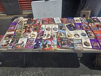 Photo of a table covered with numerous vintage romance paperback books with colorful covers illustrating couples and romantic themes.