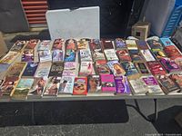 Wide view of a table displaying about 50 vintage romance paperback books arranged in rows, showing covers and spines.
