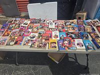 A wide table covered with approximately 45 vintage romance paperback pocketbooks.