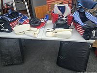 Wide view of martial arts gear laid out on table including sparring pads, protective gear, and bags