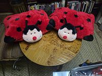 Two large red fuzzy ladybug pillows on wooden table, showing shape, colors and condition