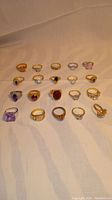 Full view of 20 rings arranged in rows, showing variety of stones and metal tones.