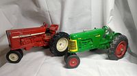 Side view of the red International and green Oliver Super 88 vintage metal toy tractors on white background.