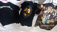 Three rock band t-shirts laid out flat: Metallica, Five Finger Death Punch, Aerosmith with vintage wear visible.