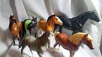 Front and side views of the six Breyer horse figurines arranged standing on white fabric background