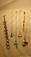 Photo showing six jewelry pieces: two bracelets and four necklaces with pendants including opal bears, turquoise cross, and charm necklace with jade.