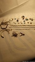 Wide view of assorted sterling silver jewelry pieces including earrings, bracelets, rings and chains arranged on a light surface.
