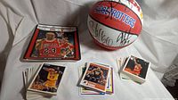 Photo showing Harlem Globetrotters signed mini basketball, Michael Jordan replica ticket plate, and multiple stacks of basketball trading cards.