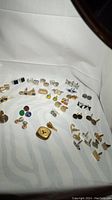 Overview of cuff links and pins arranged on white cloth showing 22 pairs