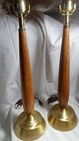 Pair of mid-century table lamps with wooden tapered bases and brass round bases shown fully.