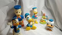 Front and angled view of six vintage Donald Duck plastic characters including bank figure and squeeze toys