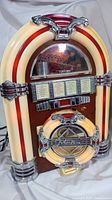 Front left perspective view of vintage jukebox styled CD radio player showing decorative illuminated columns, dome window, wood finish and round CD compartment door with chrome details