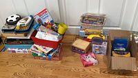 Wide shot of multiple boxes and kits stacked on floor including puzzles, craft supplies, and games.