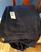 Stack of dark blue curtain panels showing faint grid pattern, folded on a chair.