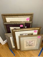 Six floral pictures stacked upright against wall showing various frame styles and sizes.