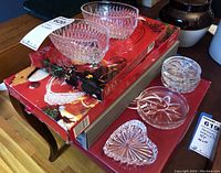 Overall display showing multiple crystal small dishes and coasters on a table with boxed Mikasa Christmas platter beneath.