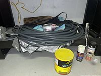 Grey coiled hoses placed on a shelf along with yellow car paint can and white Rust-Oleum spray canister with metal valve parts visible.