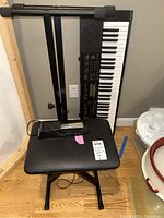 Photo showing Casio keyboard on adjustable black metal stand with bench seat in front on hardwood floor.