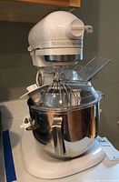 Front perspective of white KitchenAid Heavy Duty mixer with bowl and attachments on countertop