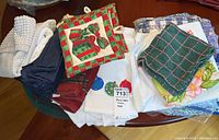 Overview of holiday-themed hand towels, heat pads, and other kitchen linens piled on a table.