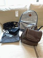 Photo of six assorted bags including backpacks and purses arranged on a sofa