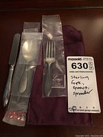 Set of 4 sterling silver utensils including 2 baby spoons, 1 baby fork, and 1 spreader displayed with plastic sleeves and note tag.