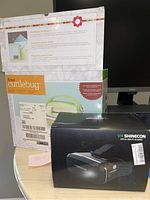 Boxes of VR Shinecon virtual reality glasses and Cricut Cuttlebug embosser and die cutter on black background.