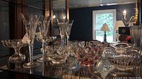 Wide view of crystal items on display including flutes, bowls, and vases in a cabinet under lighting.