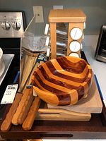 Photo showing wood-handled trays, the large wooden bowl with alternating light and dark wood stripes, wooden chopsticks, and wooden utensils placed on trays.