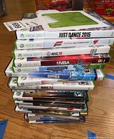 Stack of 13 Xbox 360 video games in cases, showing titles like Just Dance 2015, Forza Motorsport 4, NHL 15, NBA 2K13, Minecraft, Rapala Fishing, Sonic & All-Stars Racing Transformed, NHL 14, WWE, and Ghostbusters.