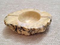 Side angle view of the handcarved alabaster ashtray showing its raw edge and carved bowl.