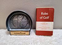 Photo showing the mini booklet titled 'Rules of Golf' next to the pewter Goodyear putting cup with a golfer relief design.