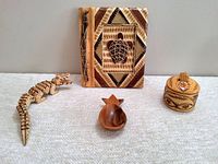 Four assorted woodcarved souvenir items on white surface: tortoise-themed photo album, crocodile figurine, trinket box, and spoon rest.
