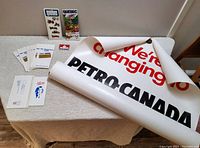 Overview photo showing large rolled paper poster partially unrolled with Fina to Petro-Canada rebranding text and various paper items on table.
