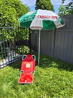 Canada Dry large advertising umbrella set up with matching red folding chair featuring Hostess Chips pail design, shown outdoors on grass.