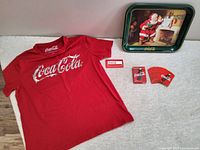 Red Coca Cola T-shirt, metal tray, and playing cards shown together
