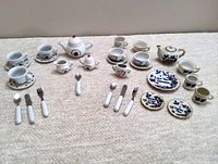 Full view of 33-piece assortment of three miniature china tea sets with ladybug and blue floral designs. Includes teapots, cups, saucers, creamers, sugar bowls (one missing lid), small plates, and utensils.
