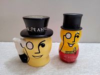 Front view of two Mr. Peanut cookie jars, ceramic and plastic, showing distinctive faces with monocles, black top hats, and smiling expressions.