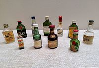 Front view of all 11 vintage 1960s airline miniature liqueur and whiskey bottles arranged in two rows on a flat surface, showing various brands and original caps.