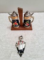 Two vintage beer stein salt and pepper shakers in wooden stand and detailed metal bottle opener shaped as a German man in traditional dress