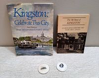 Two books on Kingston and two round pinback buttons displayed on a light carpet.