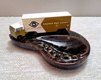 Top angle of the dark brown glazed Beauce pottery ashtray with attached United Van Lines toy van toy truck on left side.