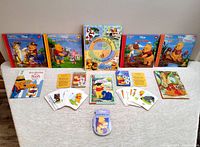Overview of all items spread out on a white cloth: 4 hardcover Disney Winnie the Pooh storybooks, teaching cards spread in piles and single cards, storybooks including one with a missing CD cover.