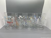 Front view of all four Disney 25th Anniversary glass tumblers showing colorful themed designs