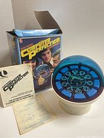 Photo showing the game unit, original box, instruction manual, and paper insert arranged on a surface.